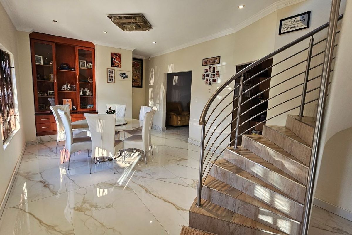 Spacious living and dining area featuring polished marble-look tiled flooring, a striking curved staircase with stainless steel railing, and built-in display cabinetry.