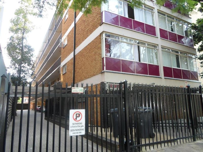 Exterior view of a multi-story apartment building featuring brick facade, enclosed balconies, and a secure gated entrance with paved driveway access.