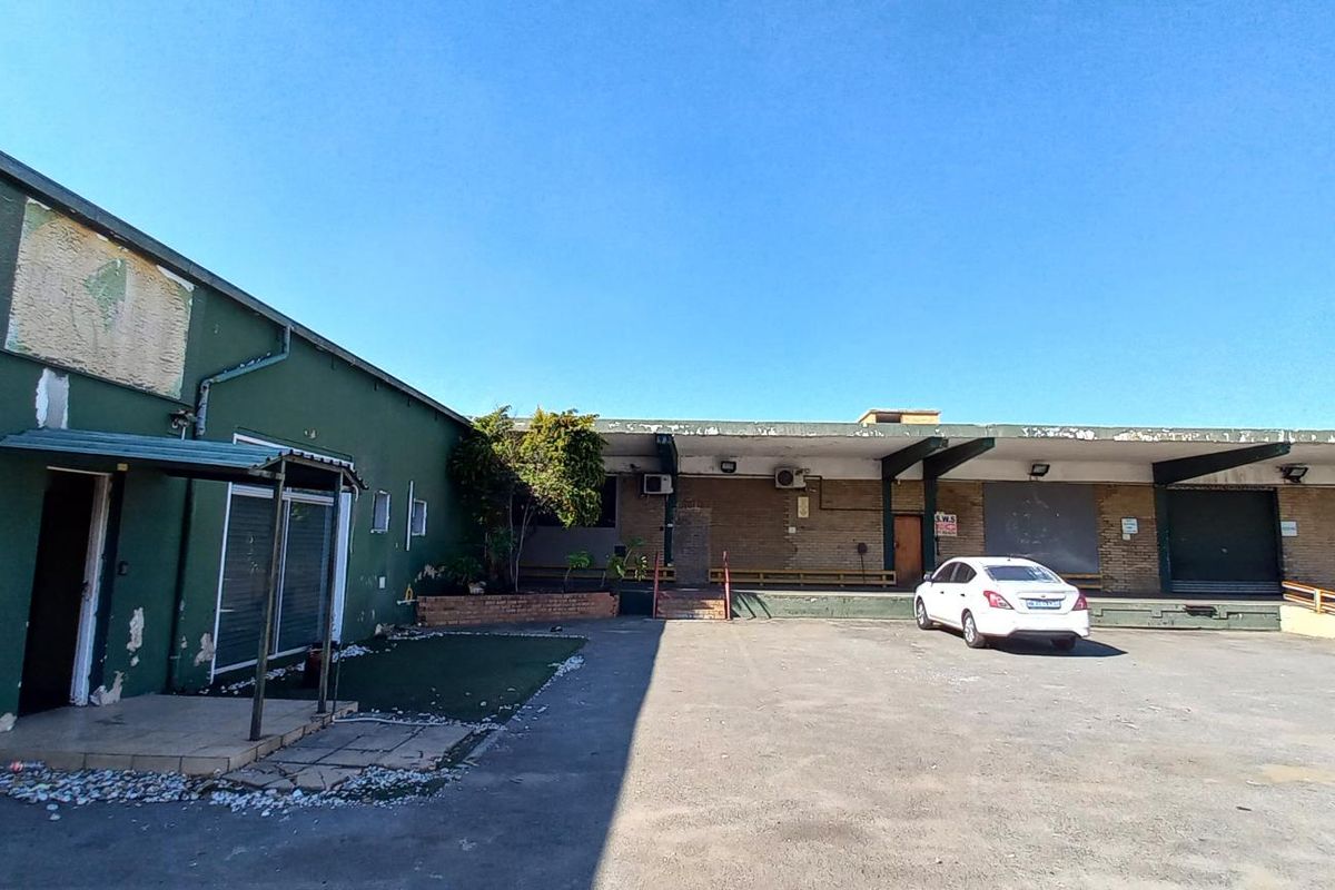 Exterior view of an industrial property featuring loading bays, roller shutter doors, and a paved yard area.