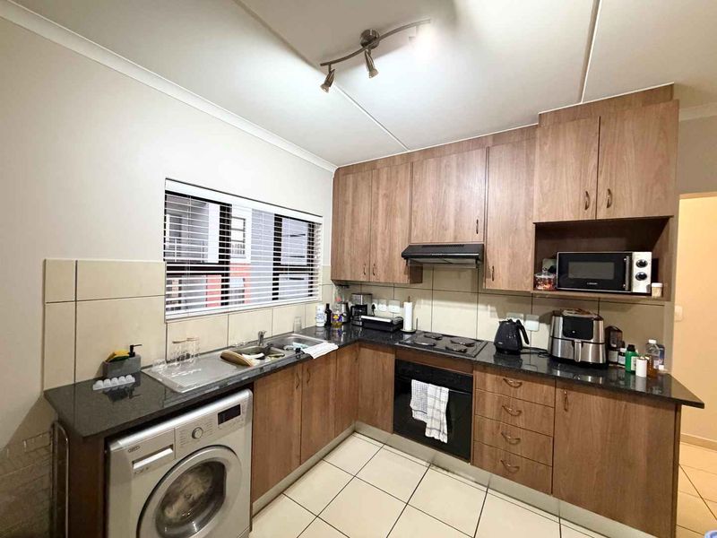 A functional kitchen featuring wood-look cabinetry, granite countertops, built-in oven, hob, extractor fan, and space for a washing machine.
