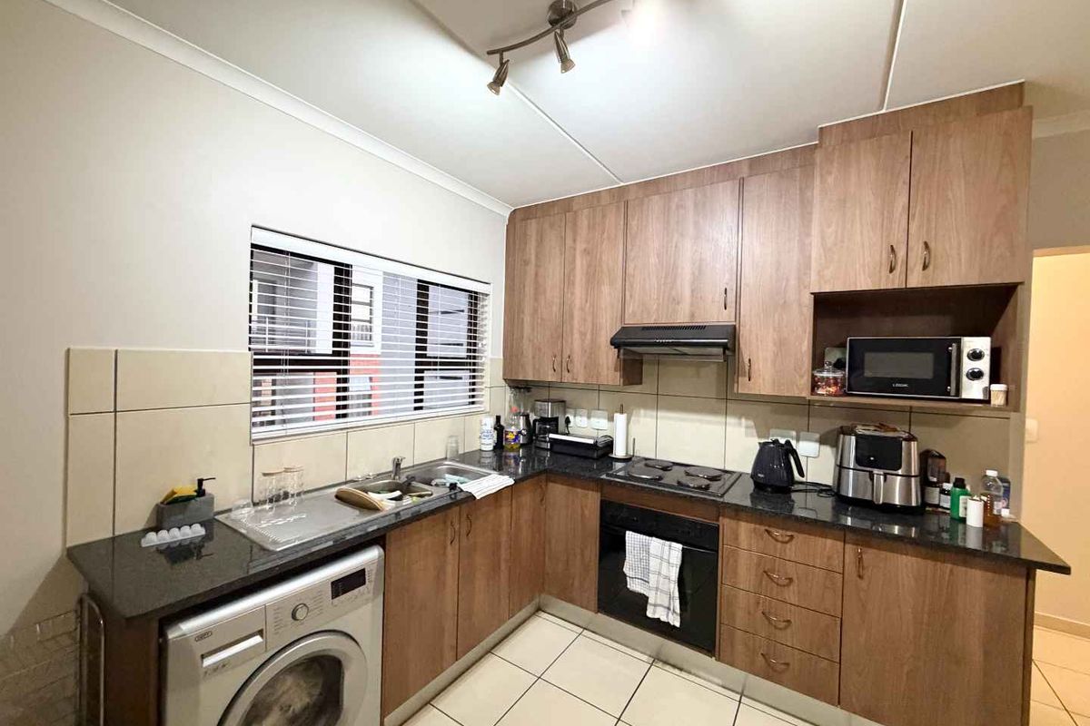 A functional kitchen featuring wood-look cabinetry, granite countertops, built-in oven, hob, extractor fan, and space for a washing machine.