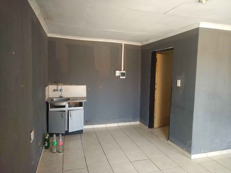 A small, basic kitchen area featuring tiled flooring, a single stainless steel sink, and base cabinetry, requiring cosmetic updates and repairs.