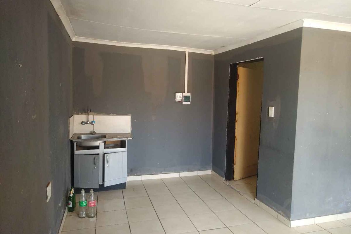 A small, basic kitchen area featuring tiled flooring, a single stainless steel sink, and base cabinetry, requiring cosmetic updates and repairs.
