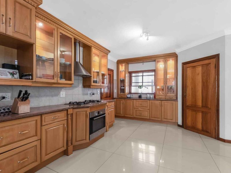A well-maintained kitchen featuring extensive wooden cabinetry, granite countertops, integrated gas hob, oven, and extractor fan, complemented by polished tiled flooring.