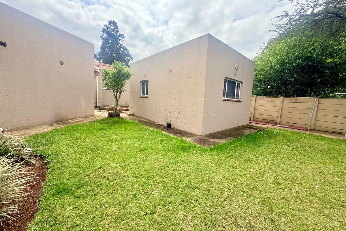 Rear exterior view of the property featuring a small lawn area, concrete pathways, and a precast concrete boundary wall.