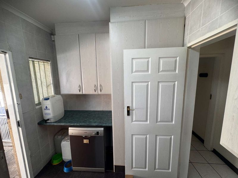 A functional laundry area featuring built-in cabinetry, tiled wall finishes, and space for a dishwasher, offering potential for modernization.