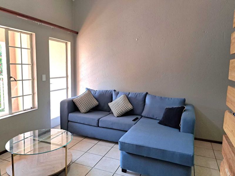A living room featuring tiled flooring, a large window, and a glass pane door providing natural light and access to the exterior.