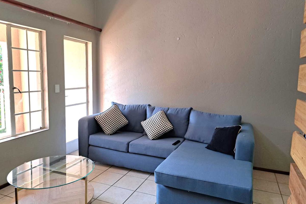 A living room featuring tiled flooring, a large window, and a glass pane door providing natural light and access to the exterior.
