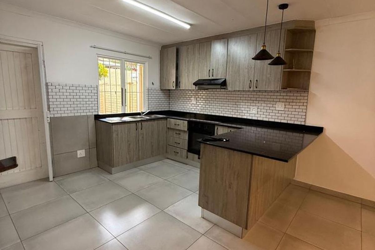 Modern kitchen featuring wood-look cabinetry, granite countertops, subway tile backsplash, and integrated appliances, offering a clean and functional workspace.