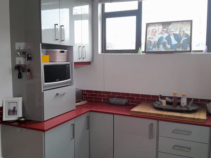 A functional kitchen featuring modern grey cabinetry, a striking red tiled backsplash, and contrasting red countertops with integrated microwave housing.