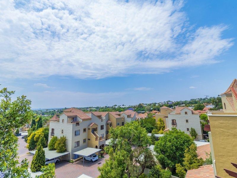 An elevated aerial view of the apartment complex, showcasing the surrounding neighborhood, tiled roof architecture, paved driveways, and established green landscaping.