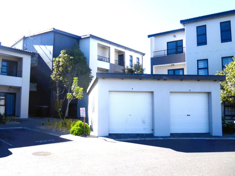 Exterior view of a modern apartment complex featuring a double garage with roller shutter doors and paved driveway access.