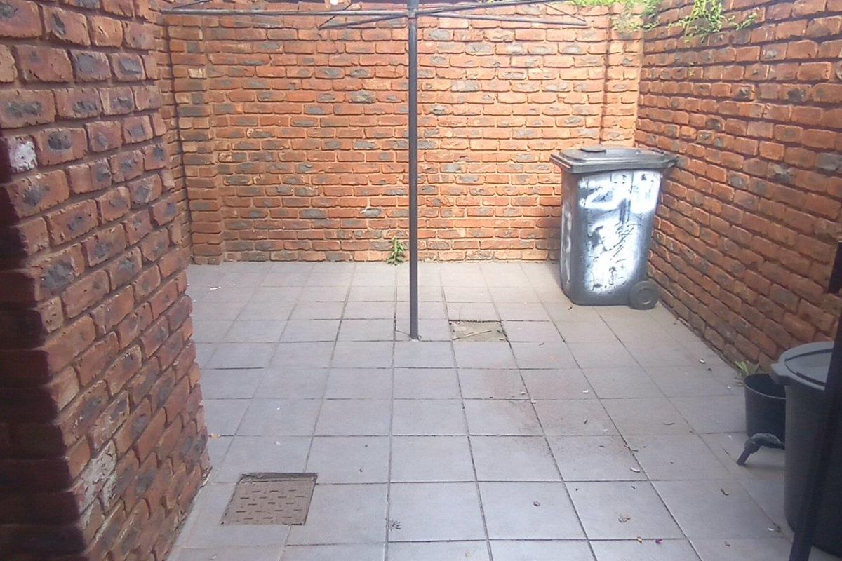 A private, enclosed courtyard area featuring exposed brick walls and paved flooring, suitable for a utility or drying space.