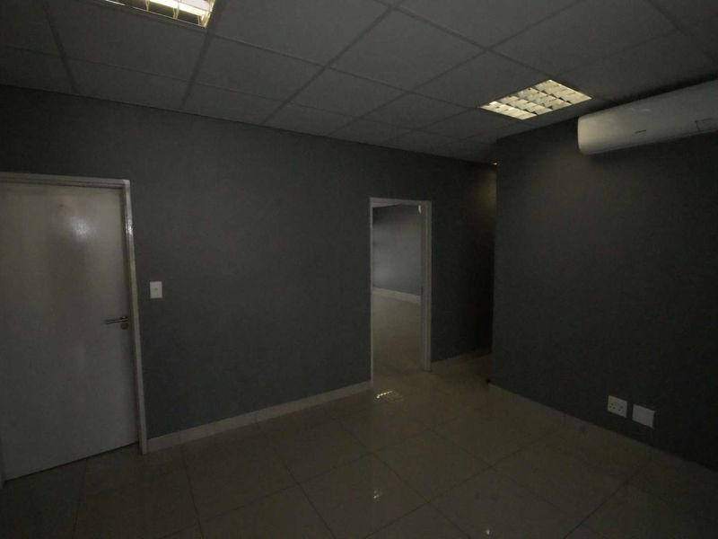 An empty office space featuring tiled flooring, a suspended ceiling with recessed lighting, and a wall-mounted split-system air conditioning unit.