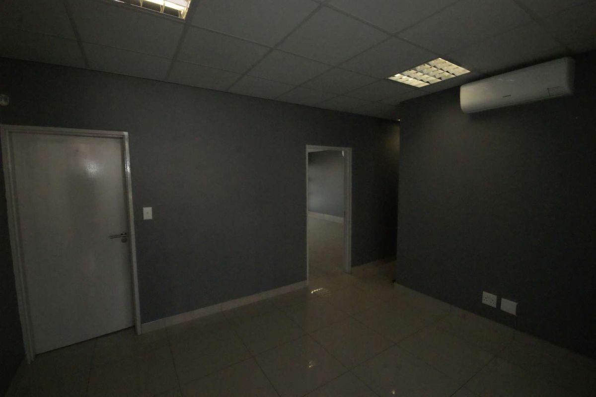 An empty office space featuring tiled flooring, a suspended ceiling with recessed lighting, and a wall-mounted split-system air conditioning unit.