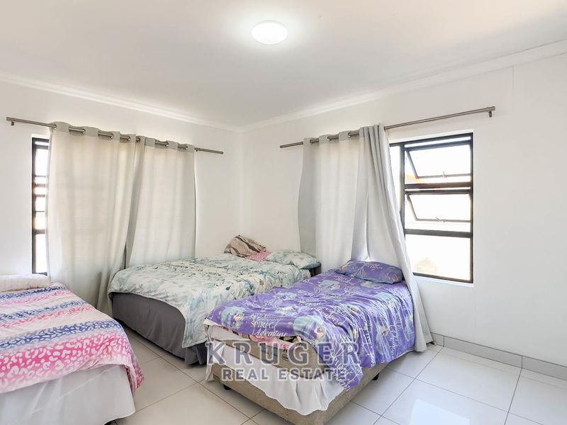 A functional bedroom featuring tiled flooring, built-in storage, and aluminium window frames, providing a clean and neutral space.