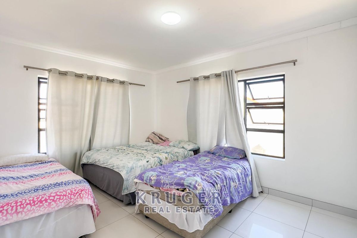 A functional bedroom featuring tiled flooring, built-in storage, and aluminium window frames, providing a clean and neutral space.