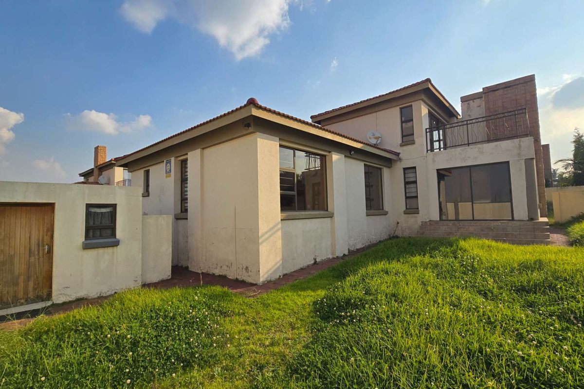 Rear view of the property featuring a balcony, sliding glass doors, and an attached storage unit, set against a large grassed garden area.