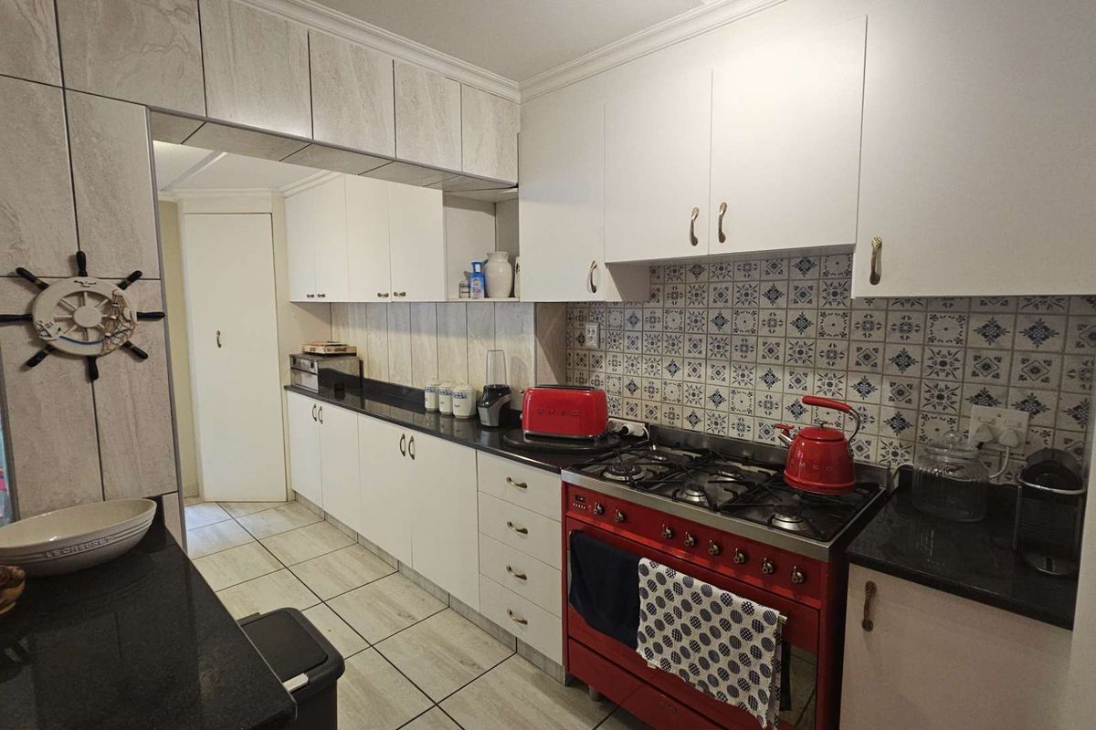A functional kitchen featuring white cabinetry, dark granite countertops, a decorative tiled backsplash, and a prominent red gas stove with an integrated oven.