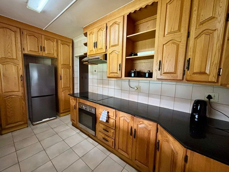 A functional kitchen featuring traditional wooden cabinetry, black granite countertops, built-in oven, and hob with a tiled backsplash and flooring.