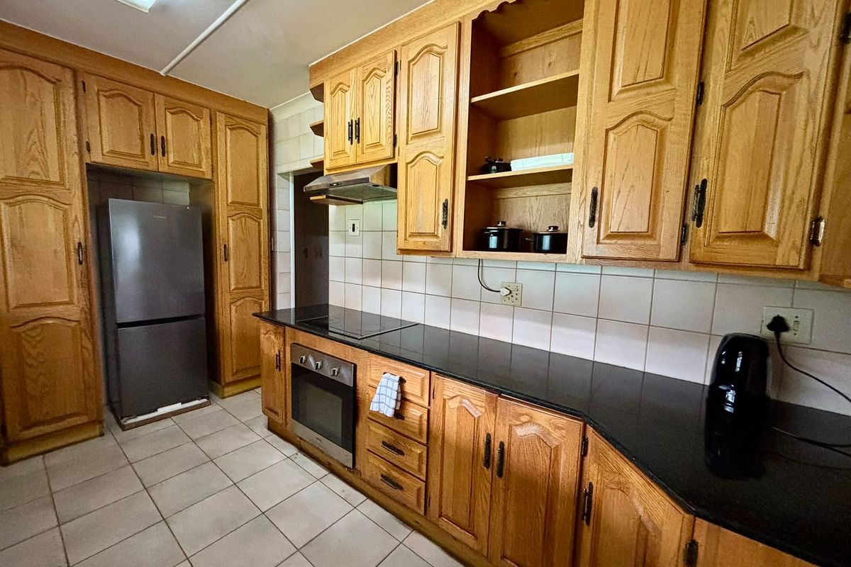 A functional kitchen featuring traditional wooden cabinetry, black granite countertops, built-in oven, and hob with a tiled backsplash and flooring.