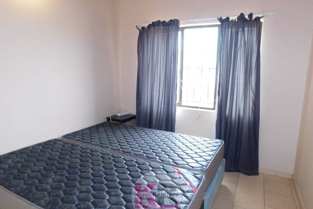 A bedroom featuring tiled flooring and a window with security bars, providing natural light to the space.
