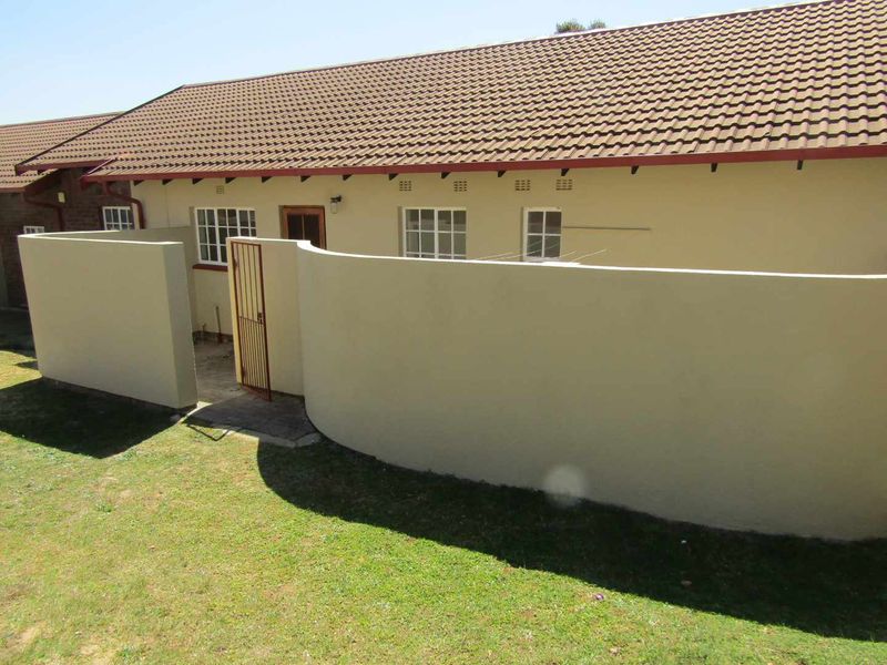 Rear view of the retirement unit featuring a private courtyard area, boundary wall, and tiled roof structure.