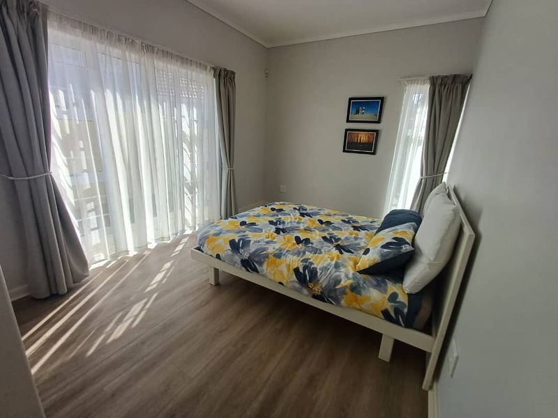 A bright bedroom featuring wood-look laminate flooring, neutral wall tones, and large sliding glass doors that provide ample natural light.