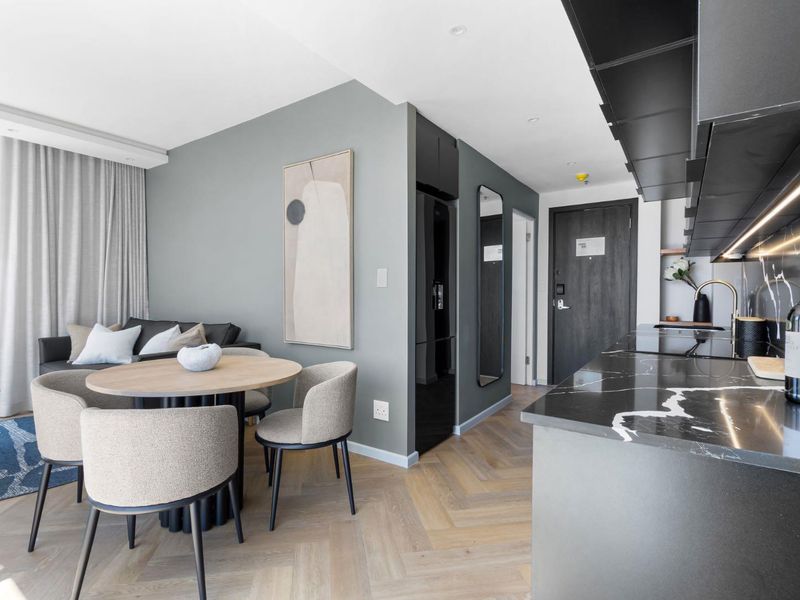 Modern open-plan living area featuring herringbone timber flooring, a sleek black marble kitchen countertop, and integrated cabinetry in a contemporary apartment setting.