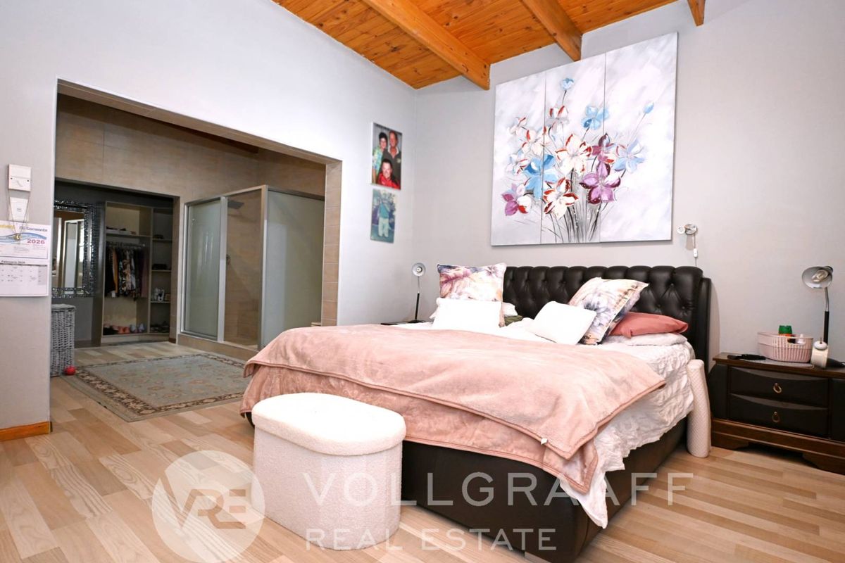 Spacious bedroom featuring exposed timber ceiling beams, light wood-look flooring, and an open-plan en-suite bathroom with a glass-enclosed shower.