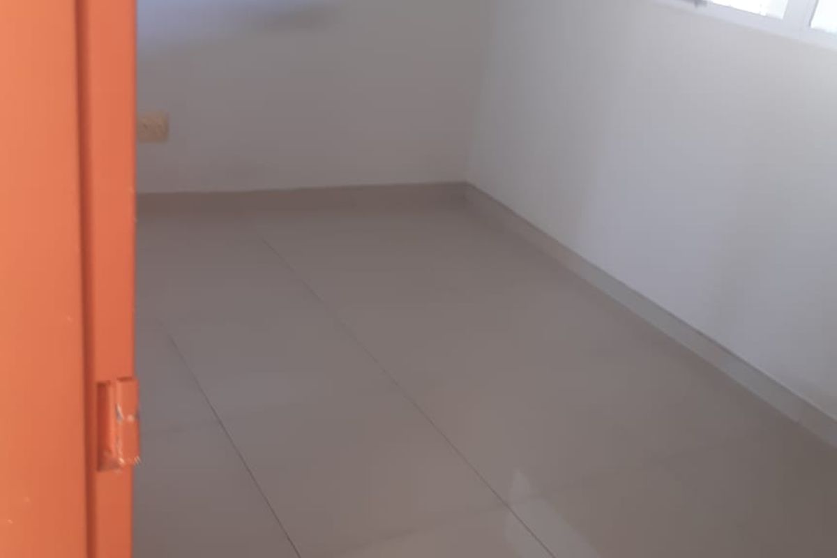 A bright, empty bedroom featuring neutral tiled flooring and a window, providing a clean and versatile space ready for personalization.