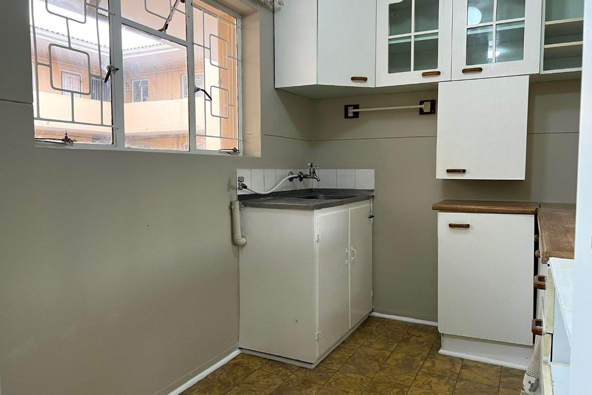 A compact kitchen area featuring built-in white cabinetry, a stainless steel sink, and tiled splashback, requiring cosmetic updates to modernize the space.