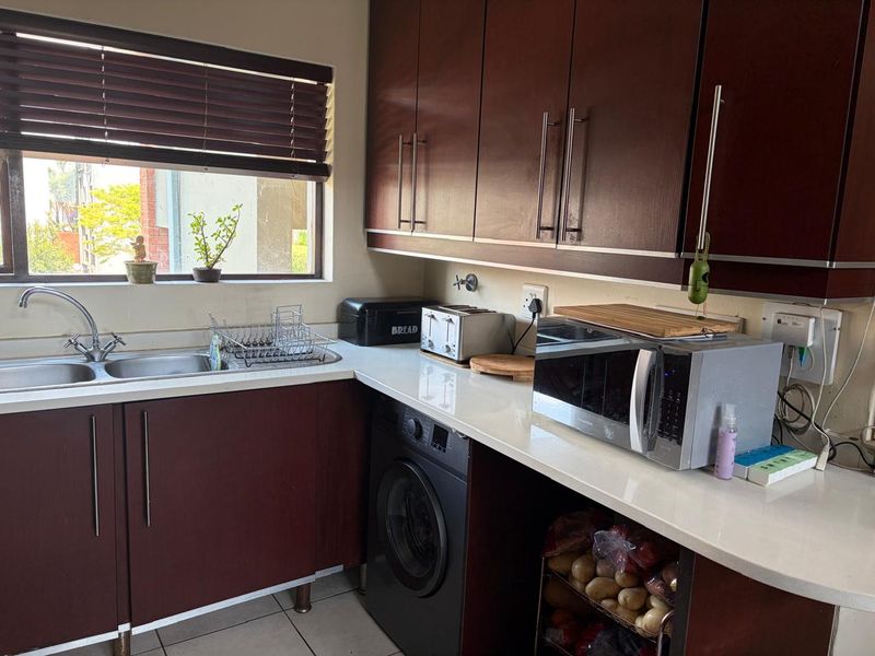A functional kitchen featuring dark wood cabinetry, white stone countertops, a double basin sink, and a built-in washing machine.