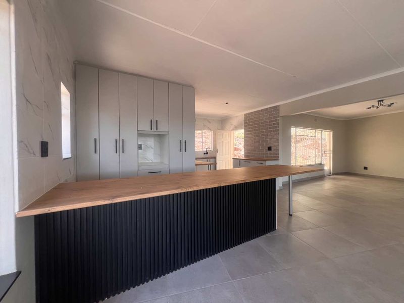 Spacious open-plan living and kitchen area featuring modern cabinetry, a large island, tiled floors, and a stylish brick feature wall.