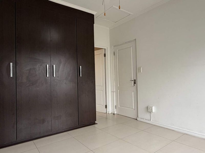A clean, empty bedroom featuring dark wood built-in cupboards, neutral tiled flooring, and white interior doors.