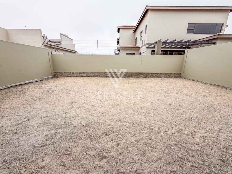 A spacious, unlandscaped rear yard area enclosed by high perimeter boundary walls, offering a blank canvas for future garden design and outdoor living space.