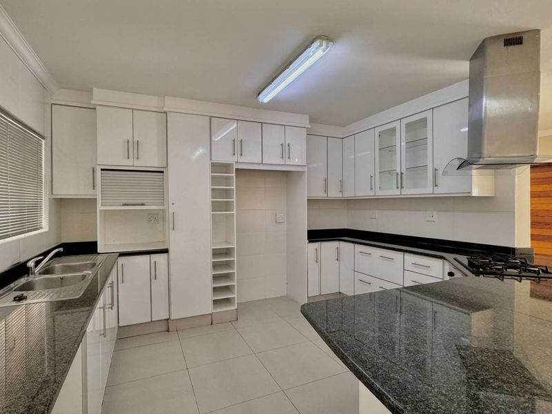 Modern kitchen featuring granite countertops, ample white cabinetry, a built-in gas hob with extractor fan, and a double bowl sink.