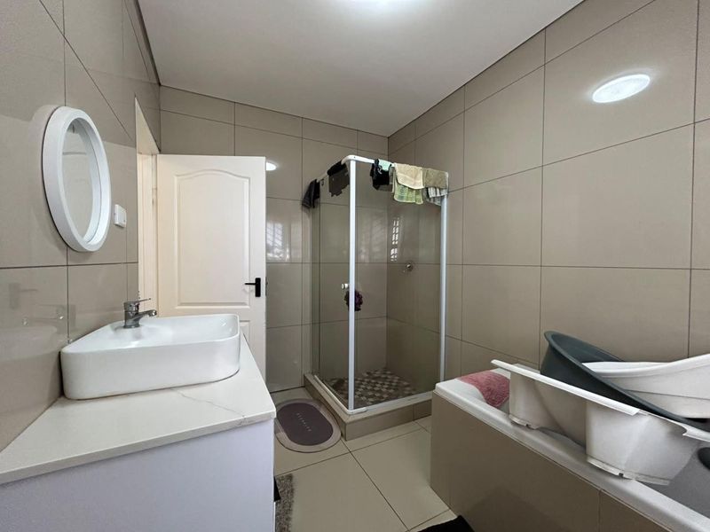 Modern bathroom featuring a vanity basin, a glass-enclosed shower, and a bathtub with neutral wall and floor tiling.