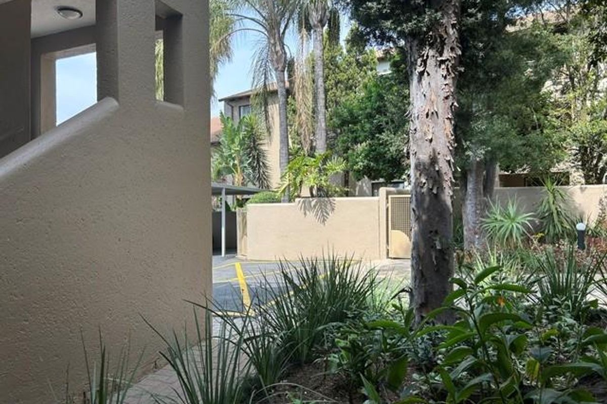 A view of the apartment complex exterior featuring a paved walkway, landscaped garden area, and surrounding boundary walls.