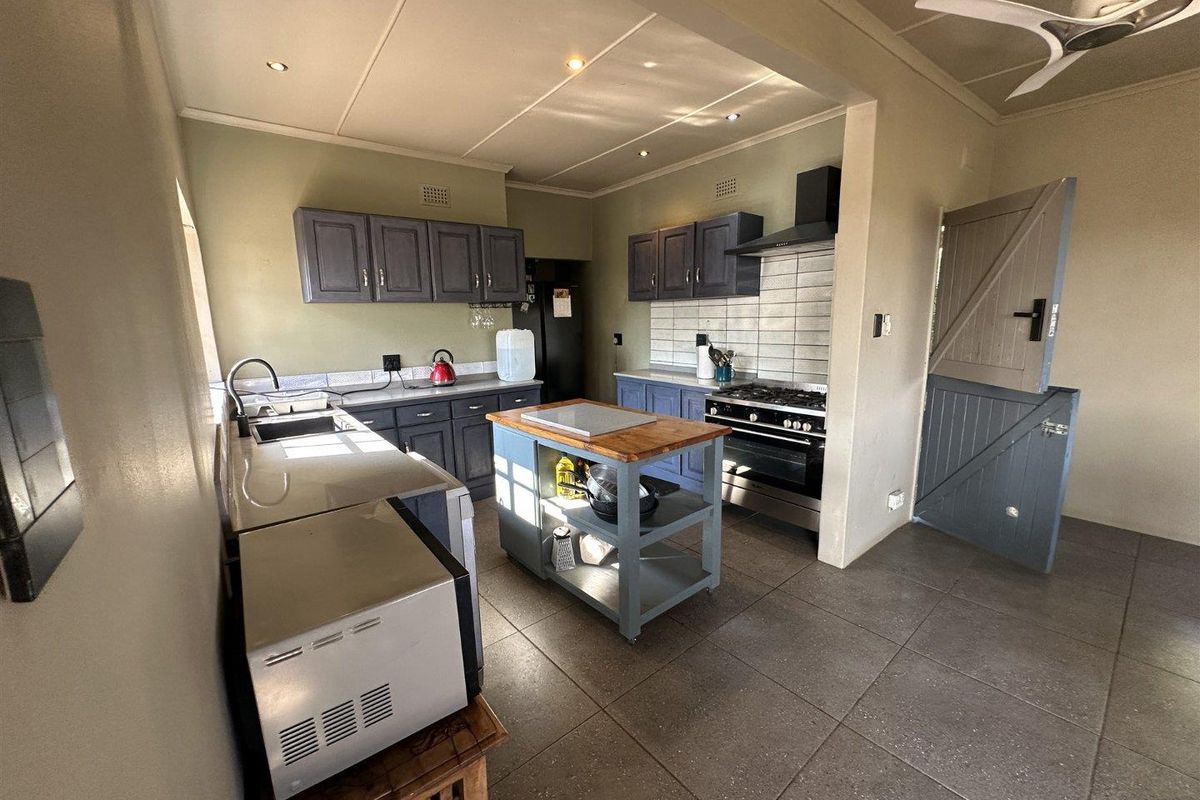 A functional kitchen featuring dark cabinetry, a gas stove with extractor, tiled flooring, and a stable door leading to the exterior.