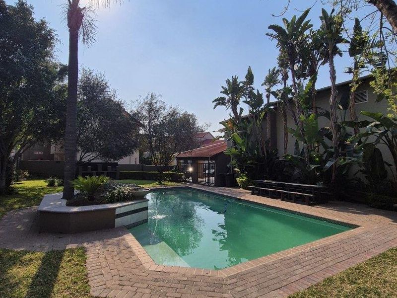 A well-maintained outdoor pool area featuring brick paving, a raised garden bed, and established landscaping in a private garden setting.