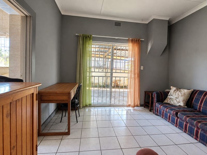 A living room featuring tiled flooring and a sliding glass door with security gate, providing direct access to the outdoor area.