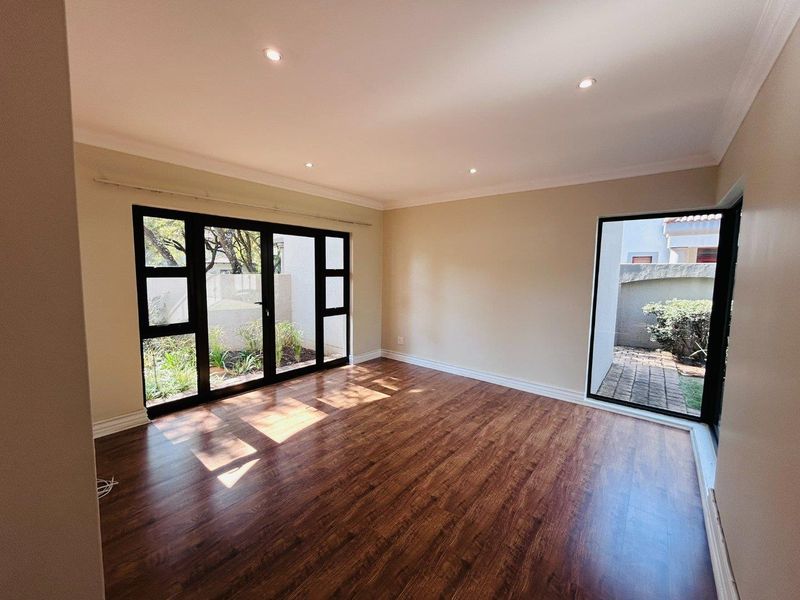 Bright and spacious living area featuring modern laminate flooring, recessed downlighting, and large black-framed glass doors providing direct access to the garden.