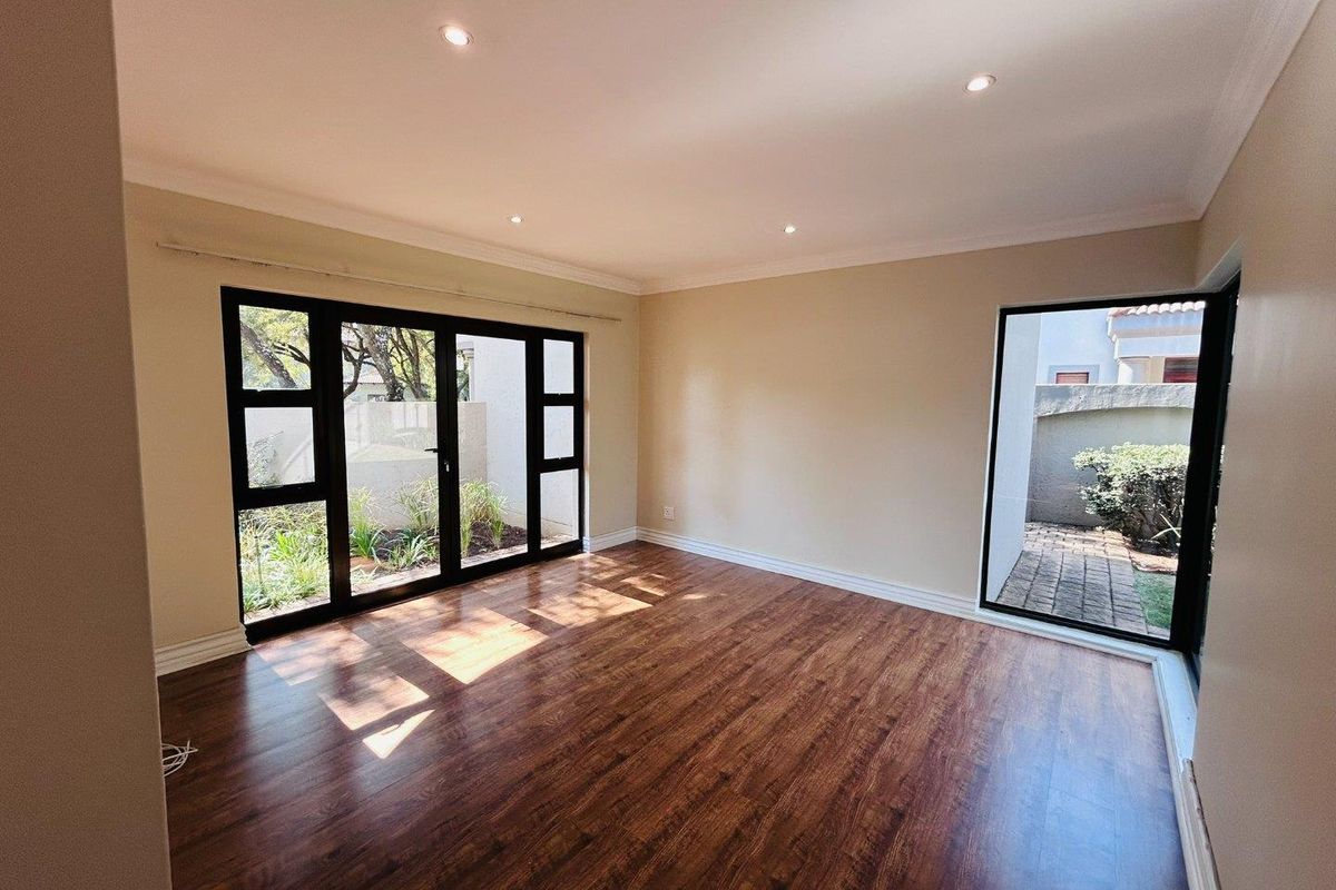 Bright and spacious living area featuring modern laminate flooring, recessed downlighting, and large black-framed glass doors providing direct access to the garden.