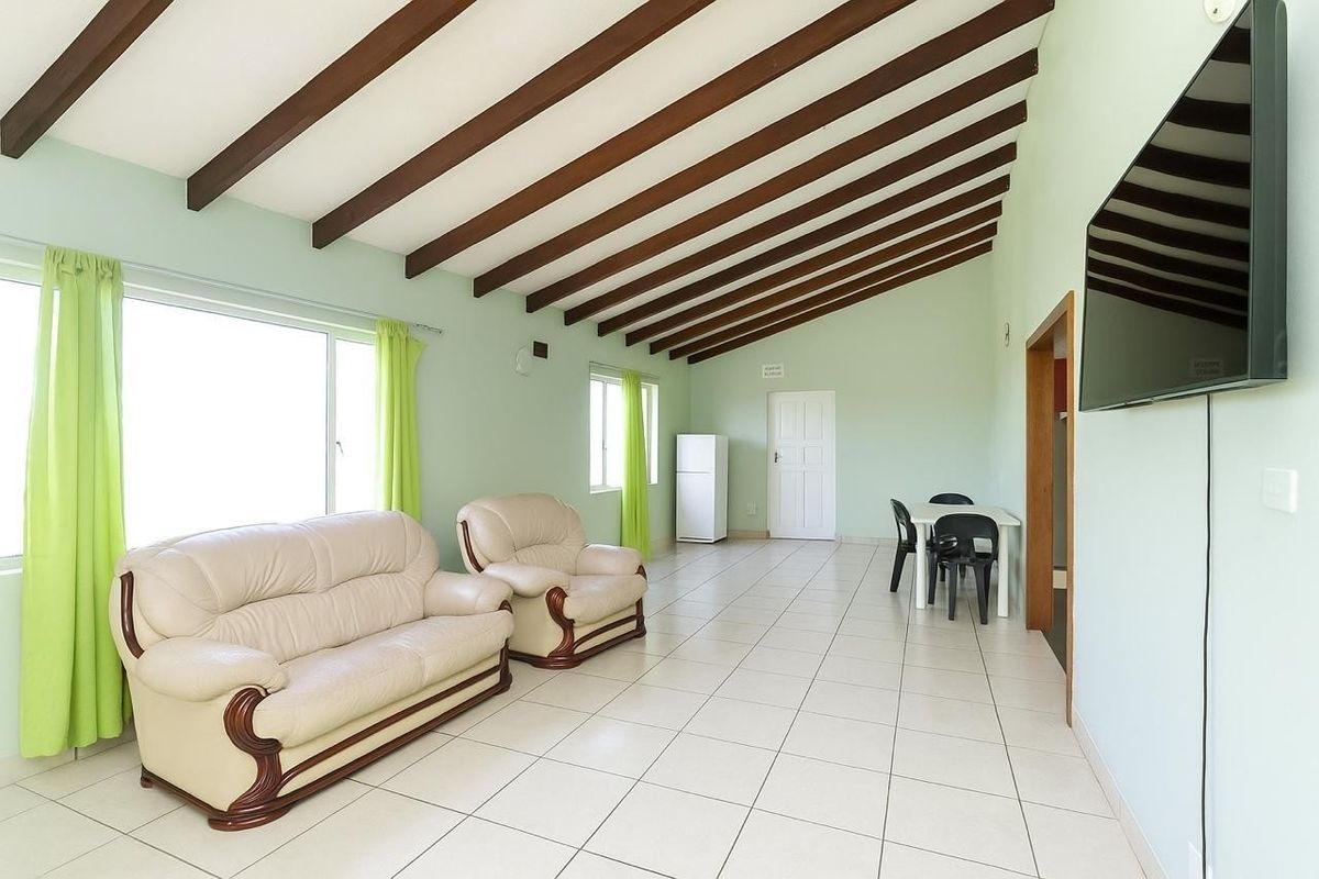 Spacious living area featuring high vaulted ceilings with exposed timber beams, neutral tiled flooring, and large windows providing ample natural light.