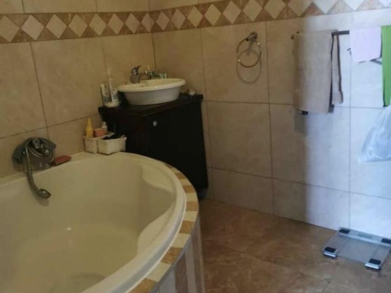 A bathroom featuring a built-in corner bathtub, a vessel sink with a vanity cabinet, and neutral wall and floor tiling.