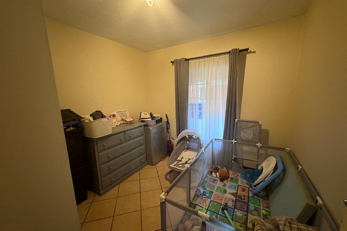 A bedroom featuring tiled flooring and a window with curtain rod, currently utilized as a nursery space.
