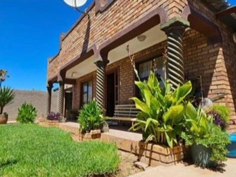 A rear exterior view of a face brick house featuring a covered patio with decorative spiral columns and a well-maintained garden area.