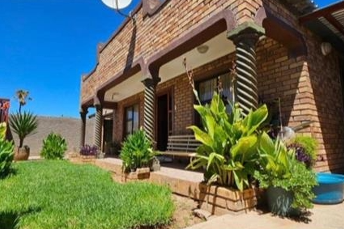 A rear exterior view of a face brick house featuring a covered patio with decorative spiral columns and a well-maintained garden area.