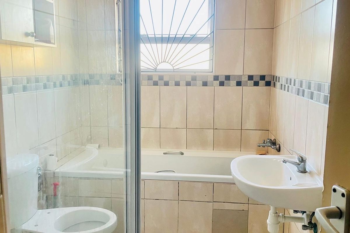 A functional bathroom featuring a built-in bathtub, glass shower enclosure, wall-mounted basin, and toilet with neutral wall tiling.